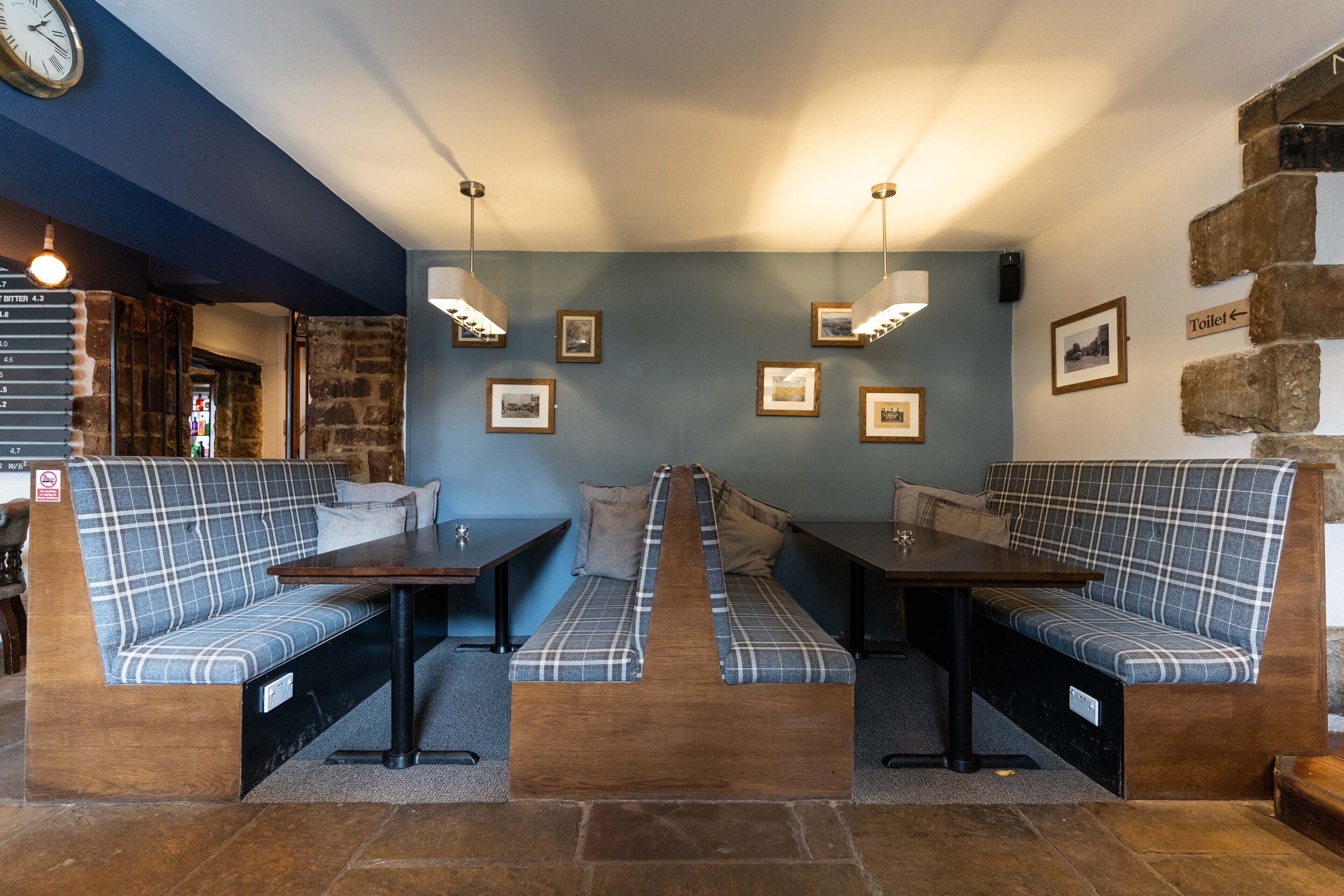 A cozy seating area with plaid sofas and tables, a clock on the wall, and framed pictures on the walls.