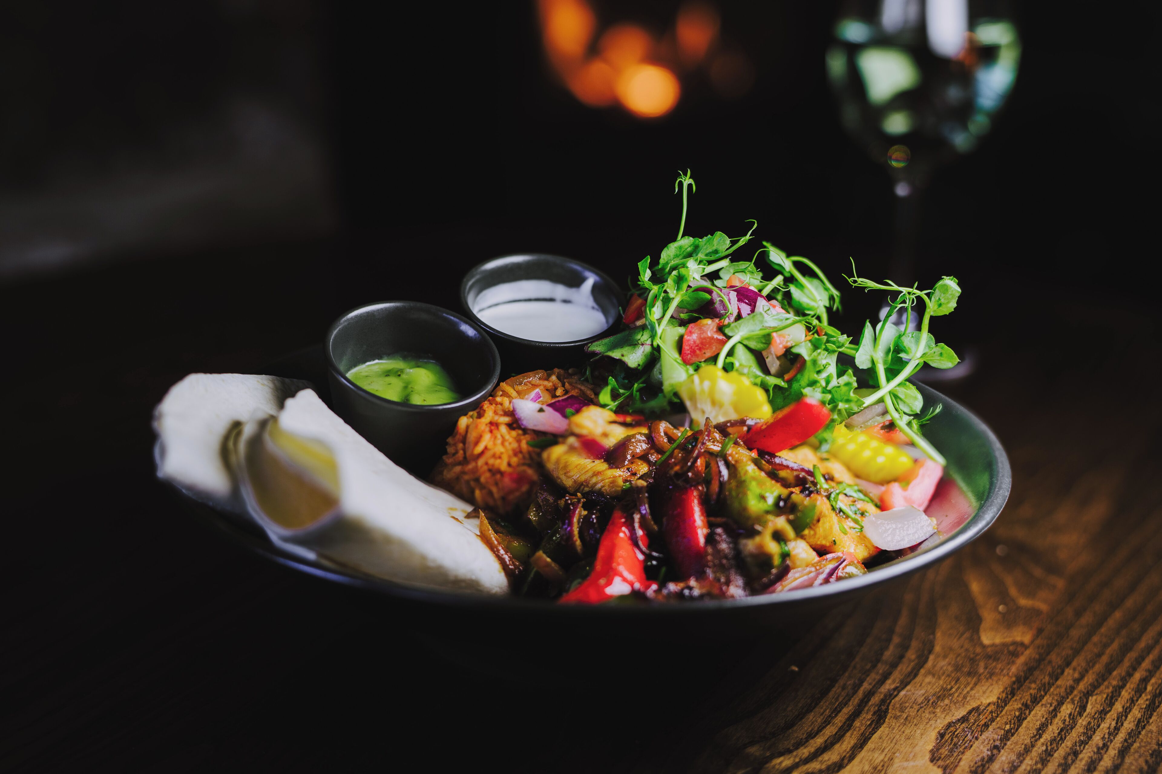 A bowl of food with various vegetables and a piece of meat, accompanied by small bowls of sauces.