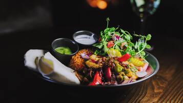 A bowl of food with various vegetables and a piece of meat, accompanied by small bowls of sauces.