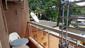 A balcony with a small table and two chairs, a satellite dish, and a view of buildings and trees. - Résidence Lumière 3 (Abidjan)