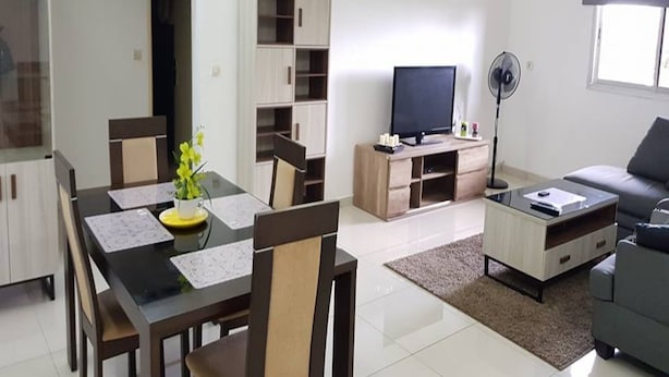 A modern living room with a dining area, a grey sofa, a TV, and a fan. - Résidence Lumière 3 (Abidjan)