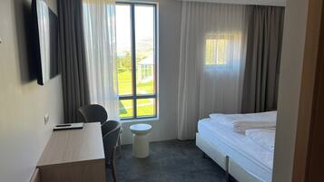Habitación de hotel con cama, escritorio, silla, mesita y televisor.