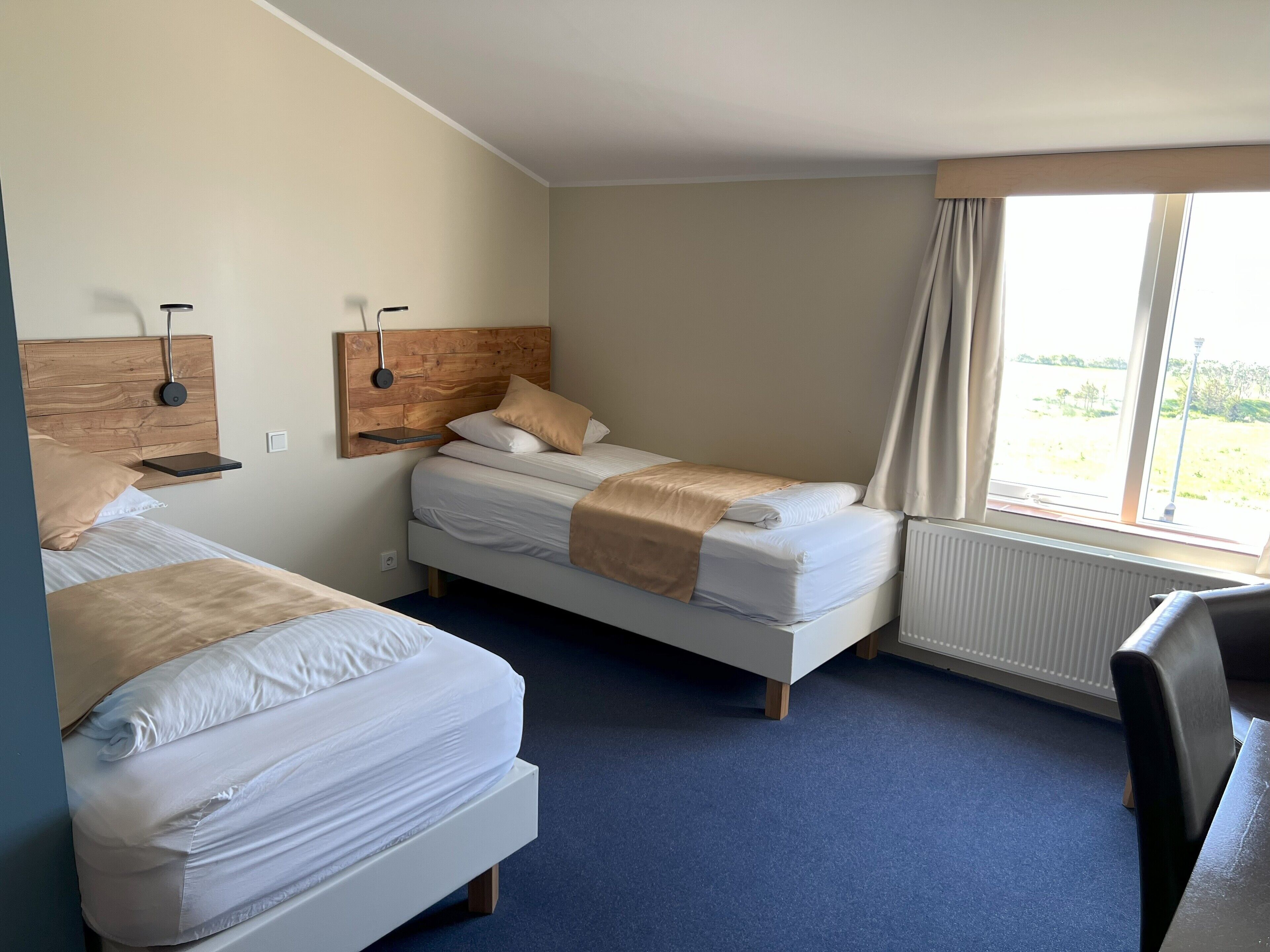 Een hotelkamer met twee bedden, een houten hoofdbord, een nachtkastje, een raam met gordijnen en een radiator.