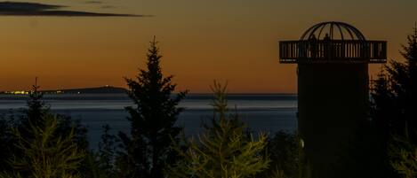 A lighthouse silhouette against a sunset sky, surrounded by evergreen trees.