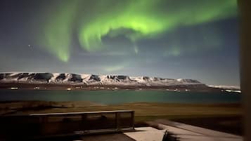 A view of a mountainous landscape with a body of water in the foreground and the Northern Lights in the background.