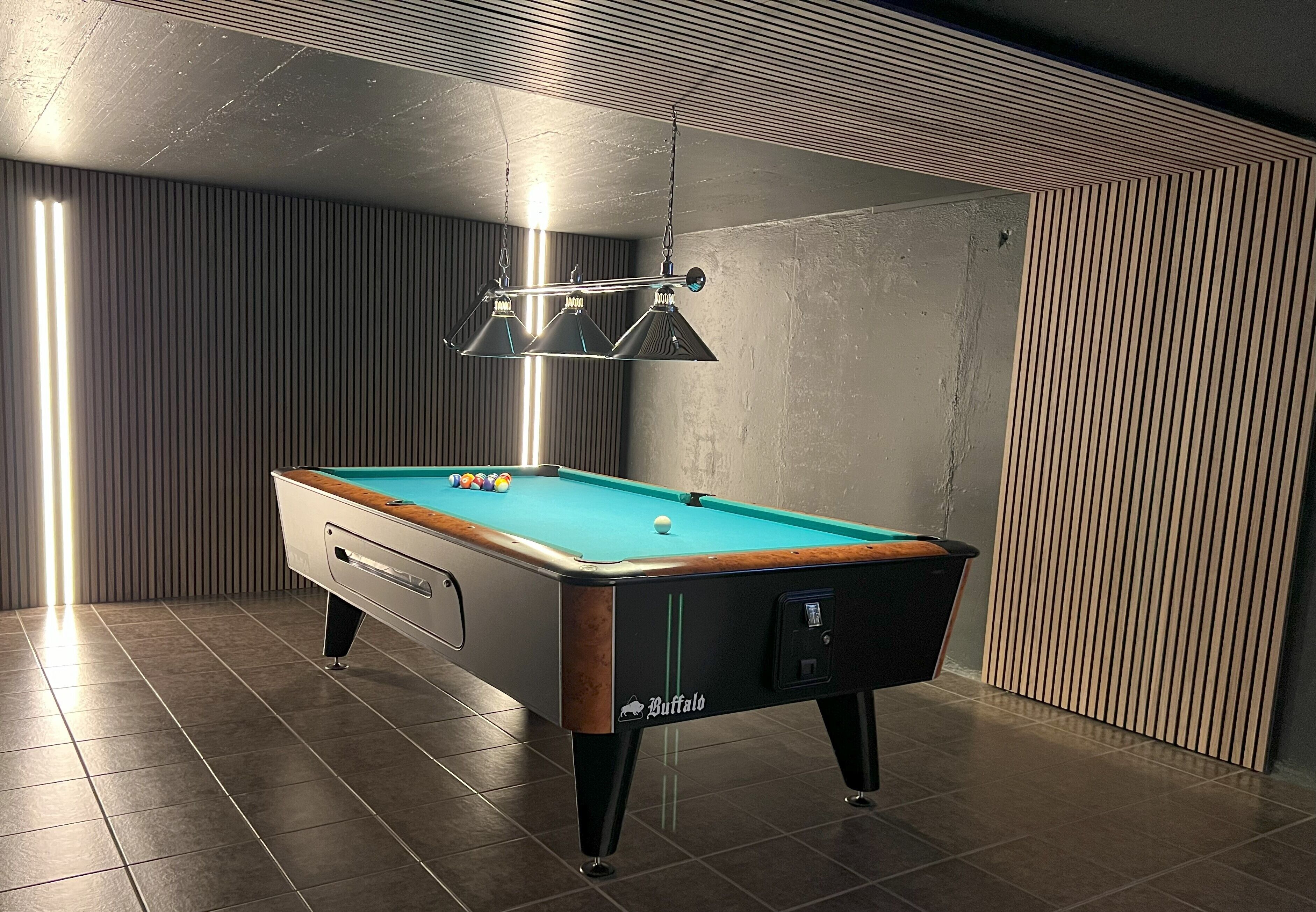 A pool table with a 'Buffalo' logo, a hanging lamp, and a textured wall.