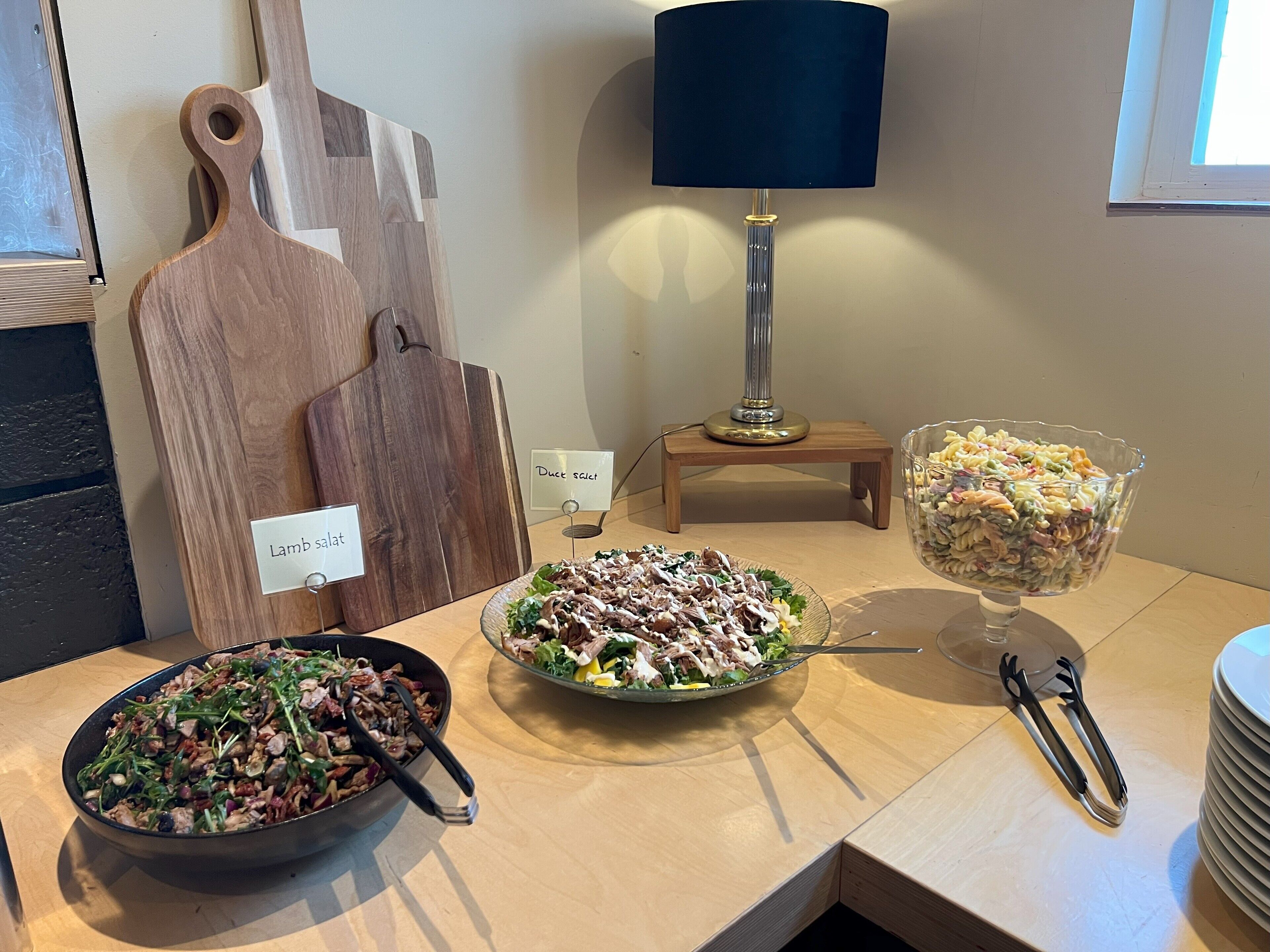 Une table à manger avec différents plats, une lampe et une planche à découper en bois avec des étiquettes.