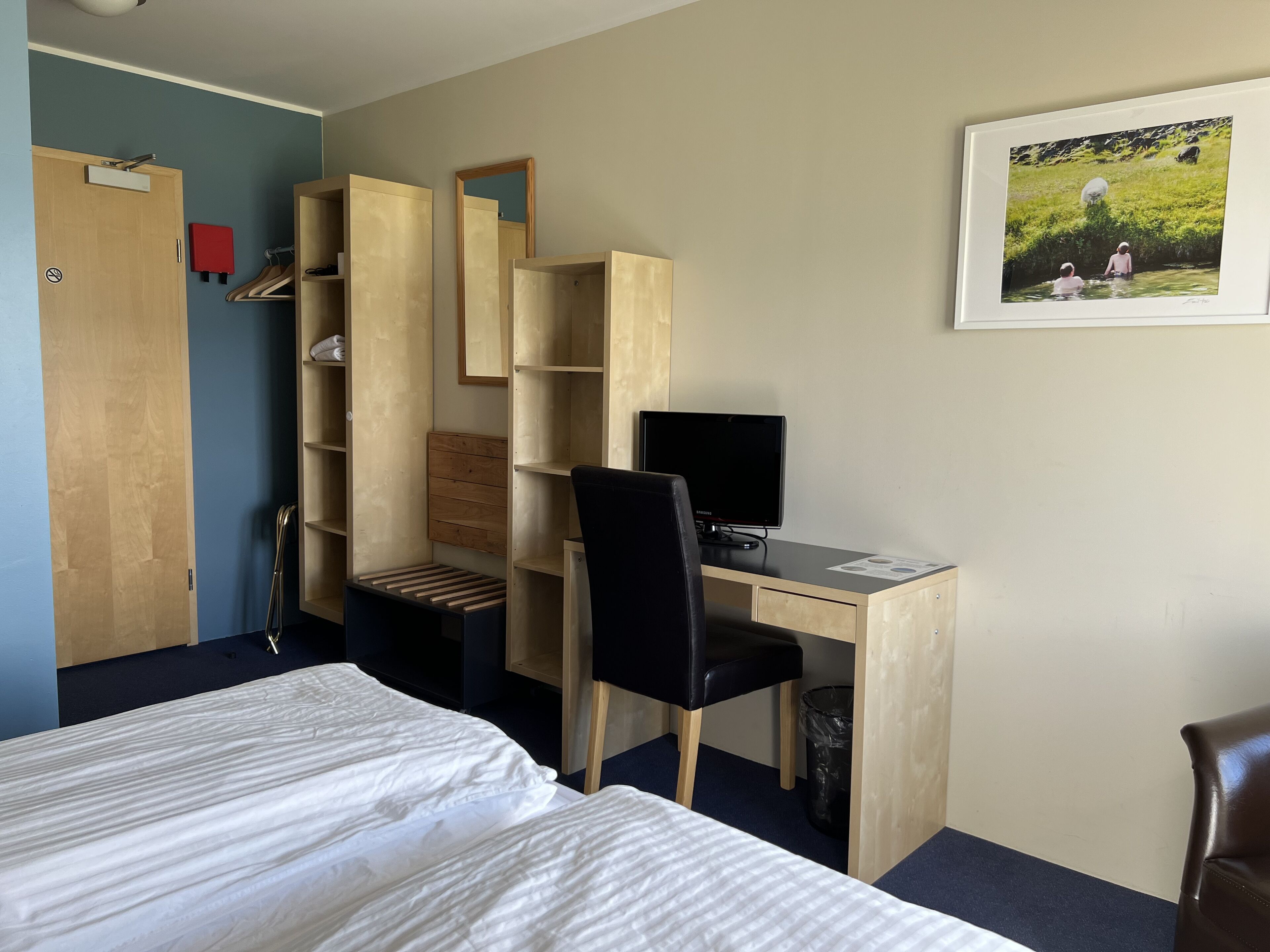 A bedroom with a bed, a desk with a computer, a chair, and a wardrobe.