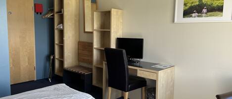 A bedroom with a bed, a desk with a computer, a chair, and a wardrobe.