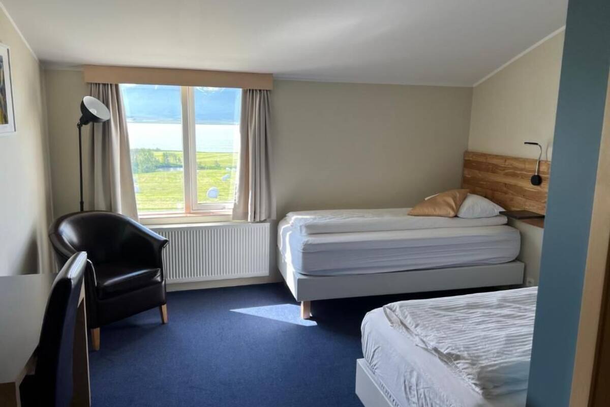 Une chambre d’hôtel avec deux lits, un bureau, une chaise et une grande fenêtre donnant sur l’extérieur.