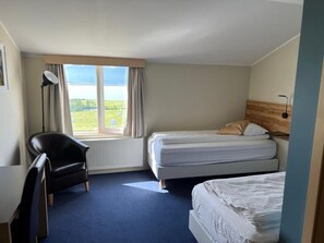 A hotel room with two beds, a desk, a chair, and a large window with a view of the outdoors. - Hotel Natur  (Akureyri)
