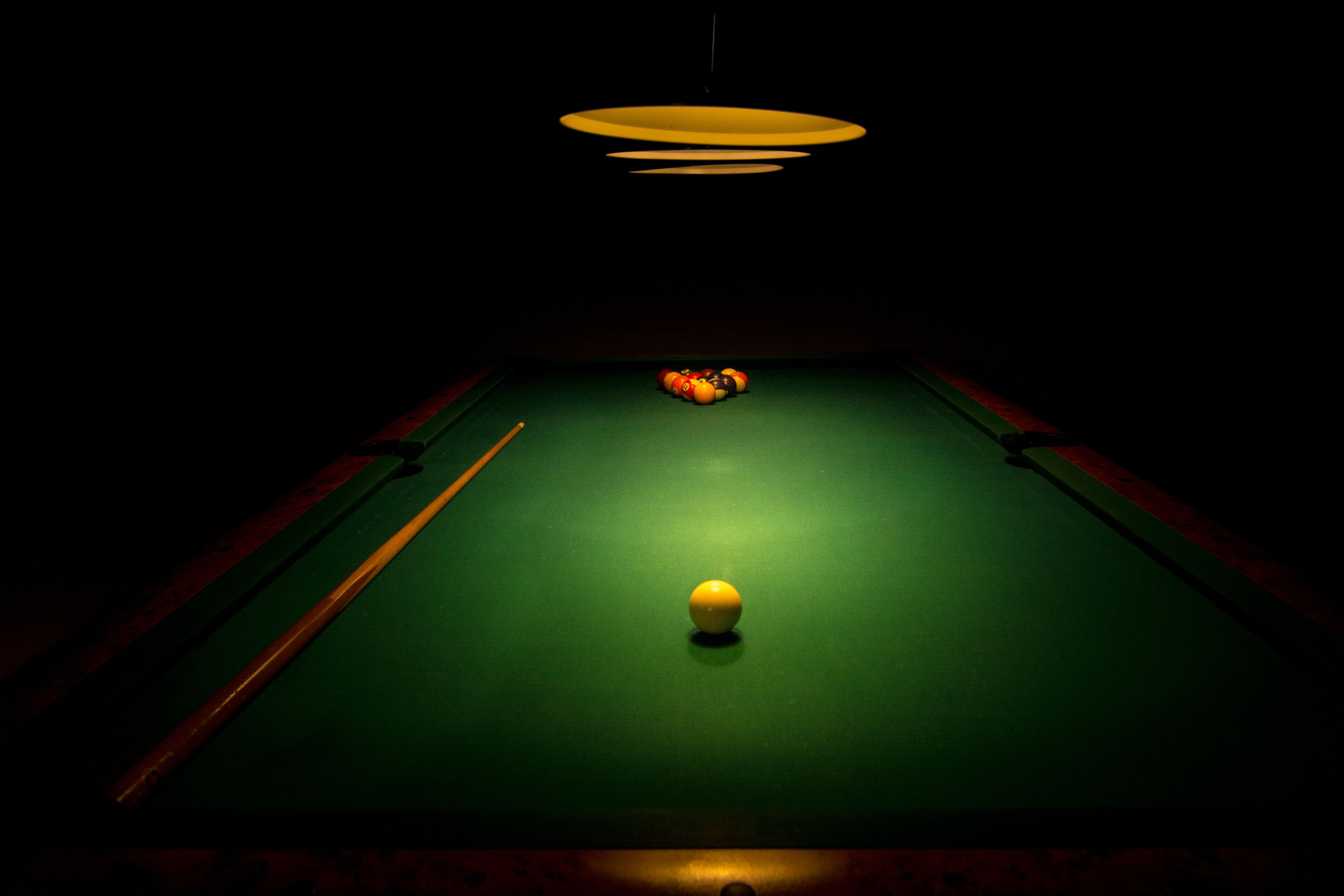 Ein Billardtisch mit Kugeln und Spielstock in einem schwach beleuchteten Raum.