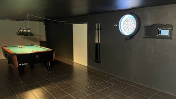 Una sala de billar con mesa de billar, dardos y luz para dardos.