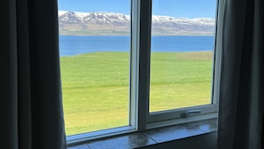 A room with a large window overlooking a grassy field and a body of water with mountains in the distance. - Hotel Natur  (Akureyri)