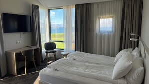 A hotel room with a bed, a desk, a chair, a TV, and a window with a view of the outdoors. - Hotel Natur  (Akureyri)