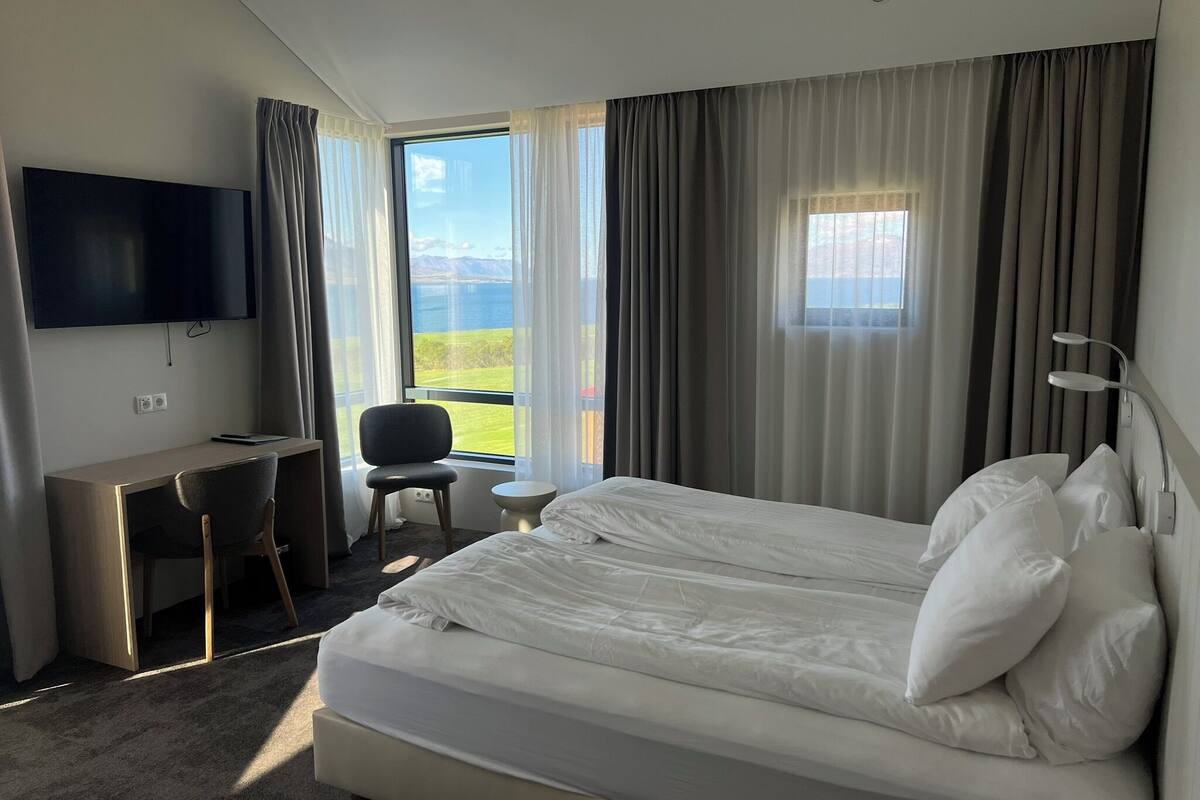 Une chambre d’hôtel équipée d’un lit, d’un bureau, d’une chaise, d’une télévision et d’une fenêtre donnant sur l’extérieur.