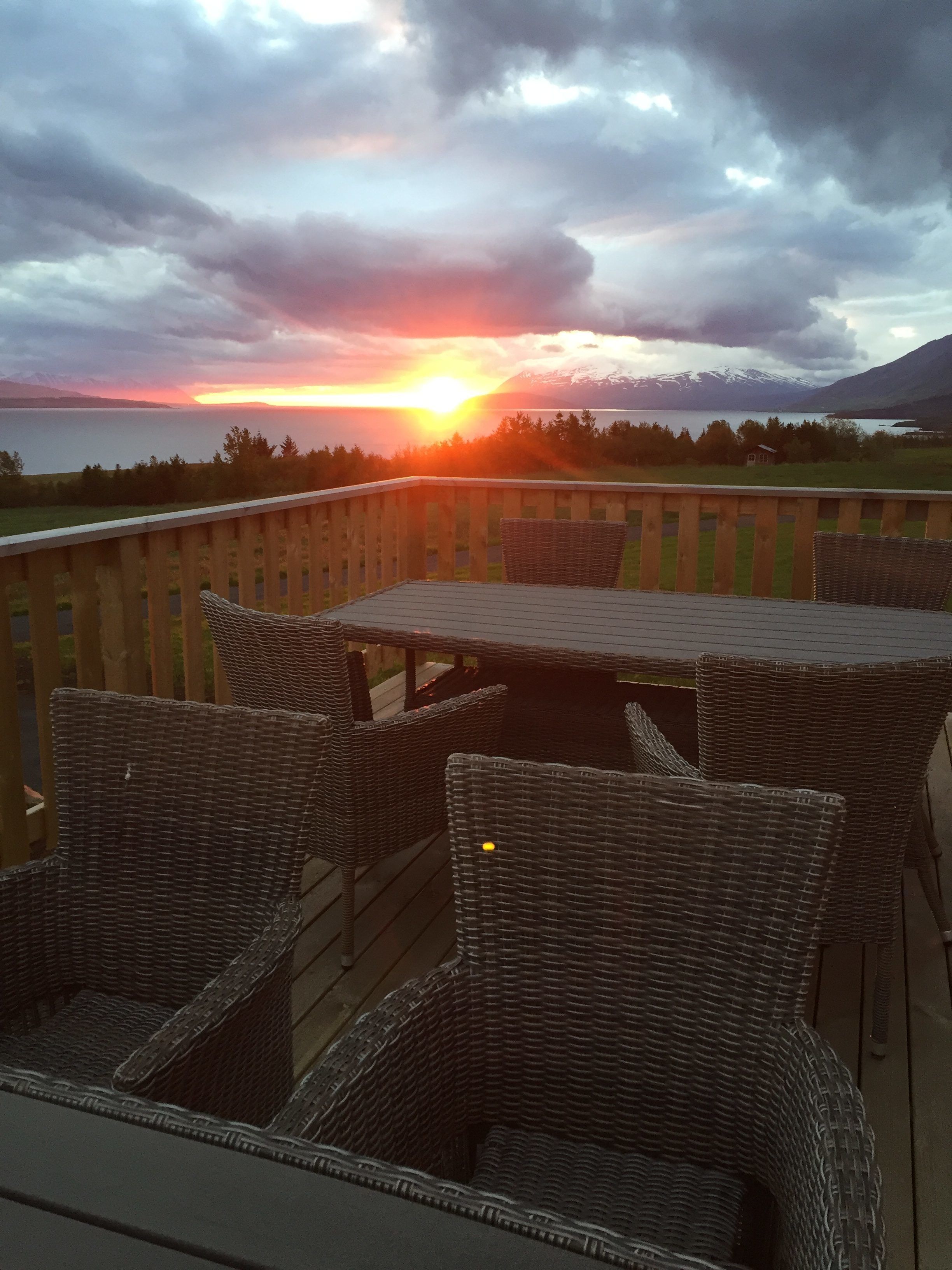 Una terraza con mobiliario de mimbre que da a una puesta de sol sobre un lago y montañas.