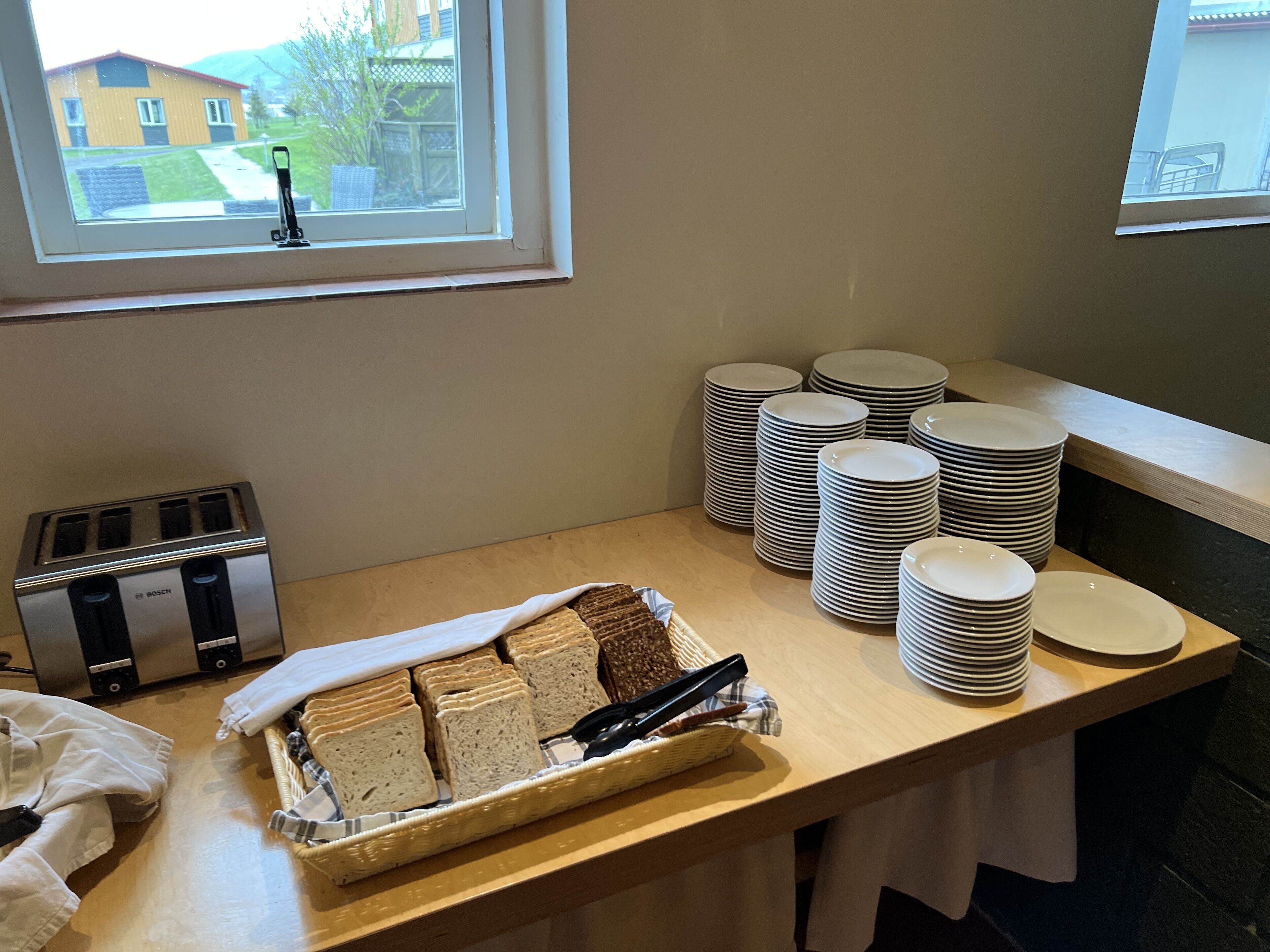 A kitchen counter with a toaster, stacks of white plates, and a basket of sliced bread.