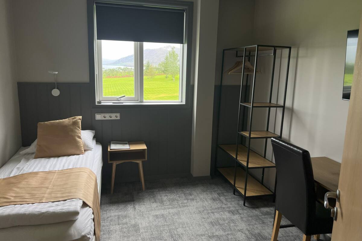Une chambre à coucher comprenant un lit, un bureau, une chaise, une armoire et une fenêtre donnant sur un paysage verdoyant.