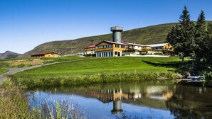A building with a tower, a pond, and a grassy area. - Hotel Natur  (Akureyri)