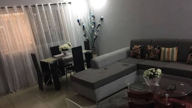 A modern living room with a grey sofa, a glass coffee table, and a dining area with a table and chairs. - Residence Vanessa (Abidjan)