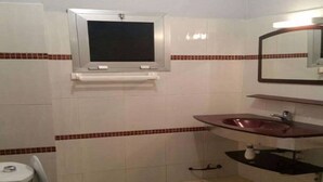 A bathroom with a toilet, sink, mirror, and tiled walls. - Residence Vanessa (Abidjan)