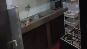 A compact kitchen with a sink, a microwave, and a gas stove. There is a small cabinet above the sink and a shelf with dishes. - Residence Vanessa (Abidjan)