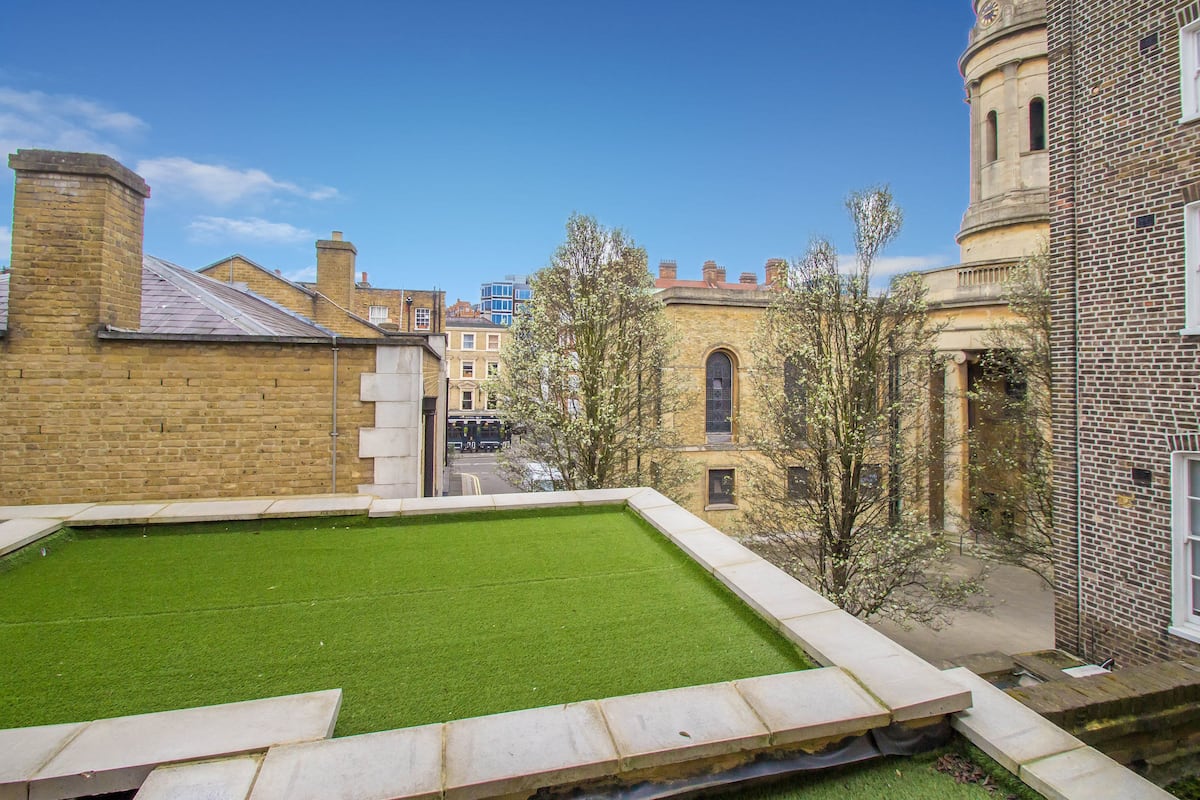 A courtyard with a green lawn, brick buildings, and a tower.