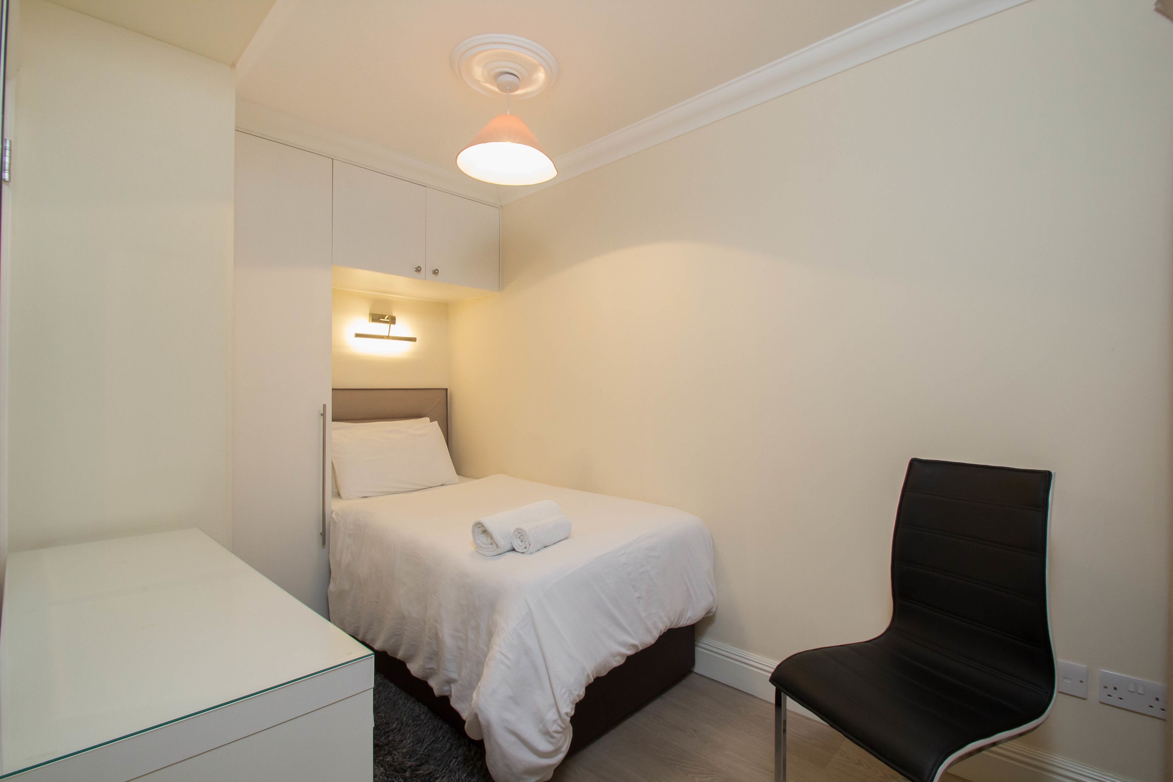 Una camera da letto piccola e curata, con un letto singolo, una sedia e un comodino.