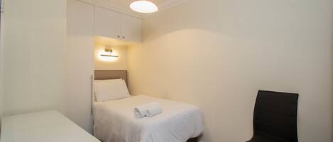 Una camera da letto piccola e curata, con un letto singolo, una sedia e un comodino.