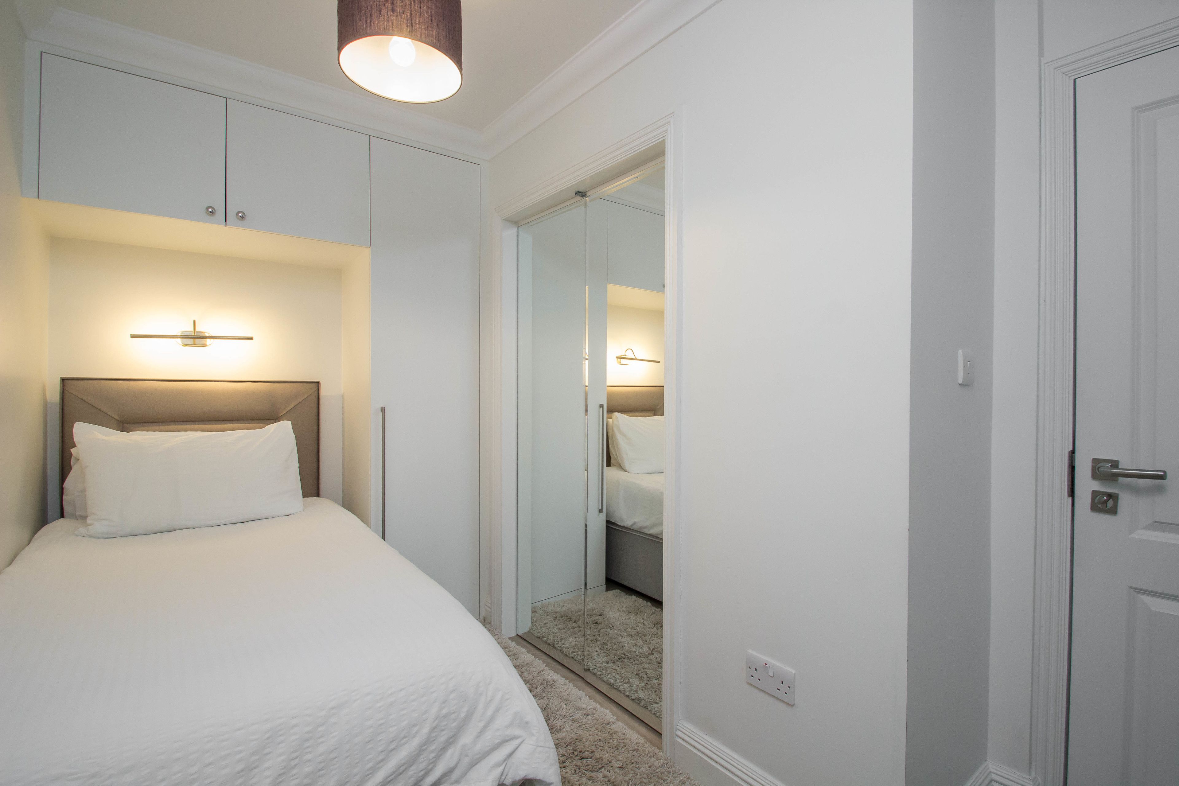 Quarto com cama, guarda-roupa, espelho e porta.
