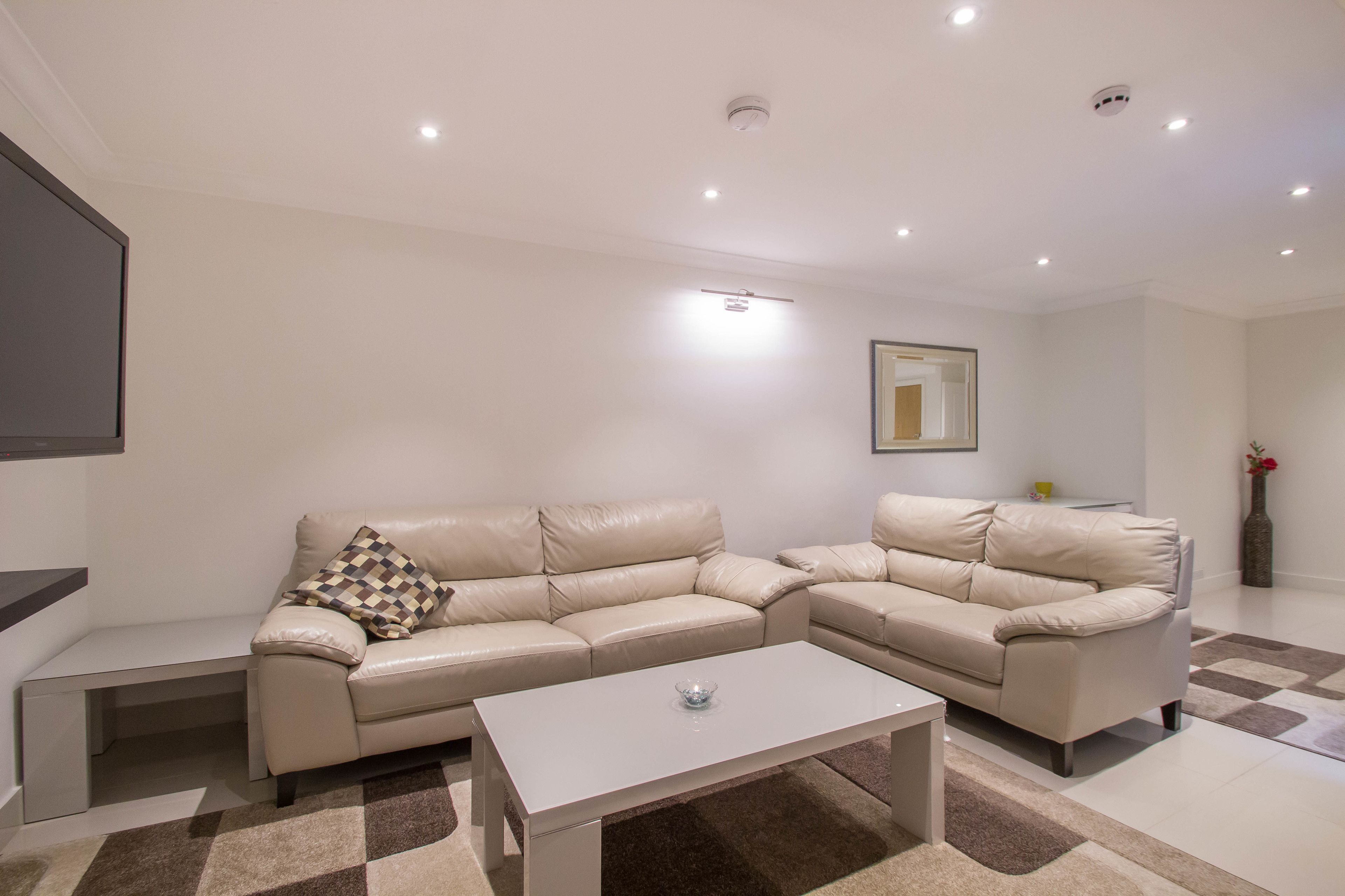 Un salon moderne avec un canapé d’angle beige, une table basse blanche et un coussin à motifs à carreaux.