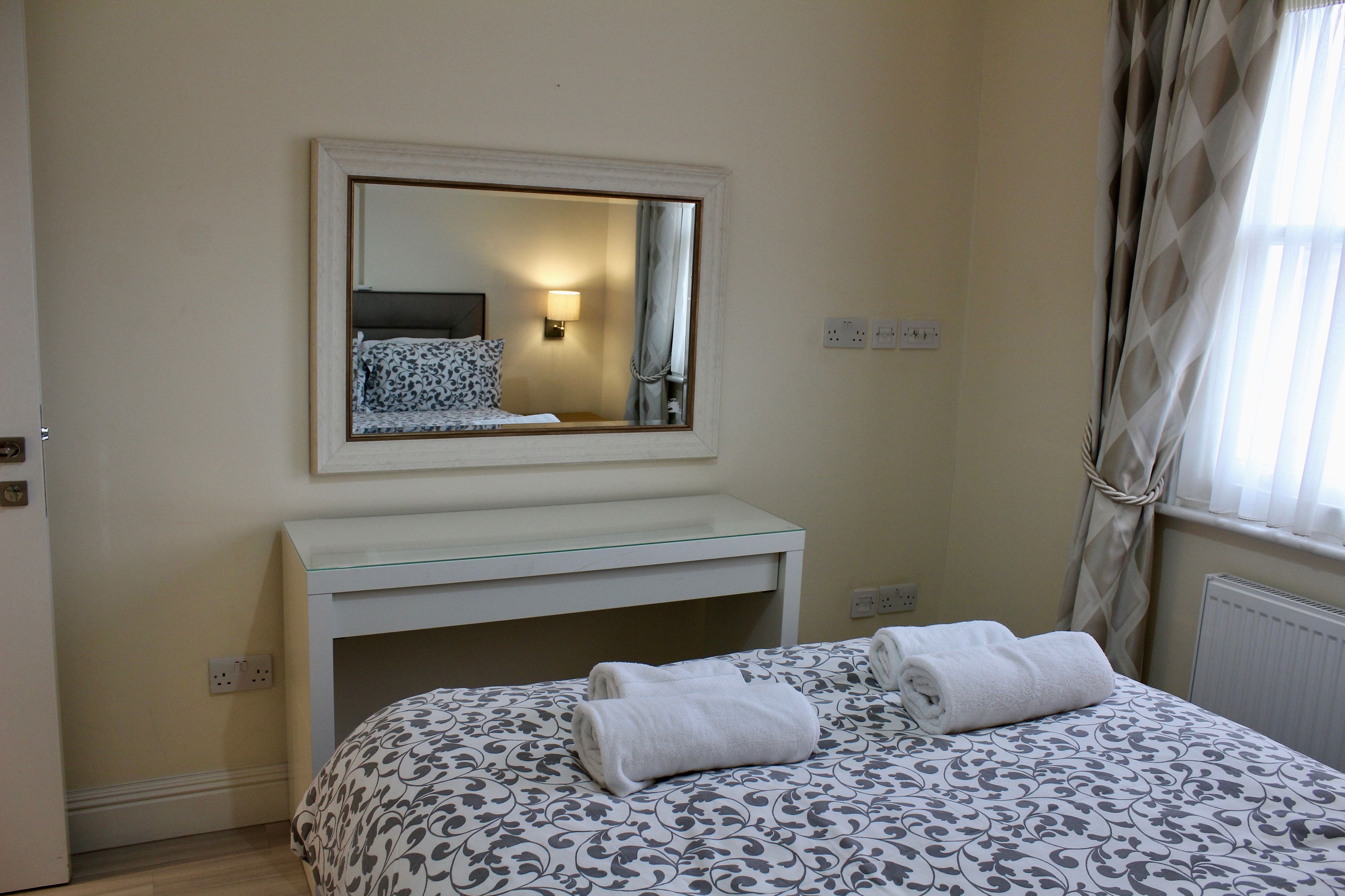 A bedroom with a bed, a bedside table, a mirror, and a window with curtains.