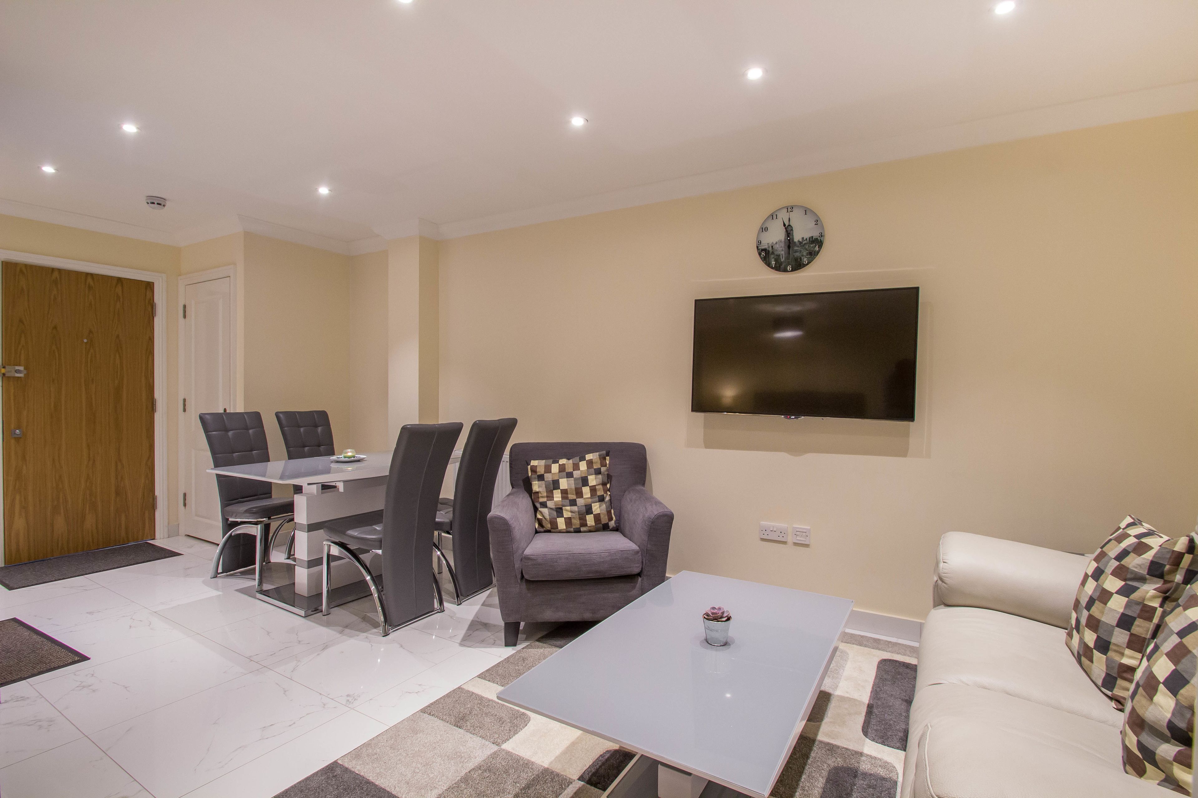 A modern living room with a dining area, a sofa, a coffee table, and a flat-screen TV mounted on the wall.