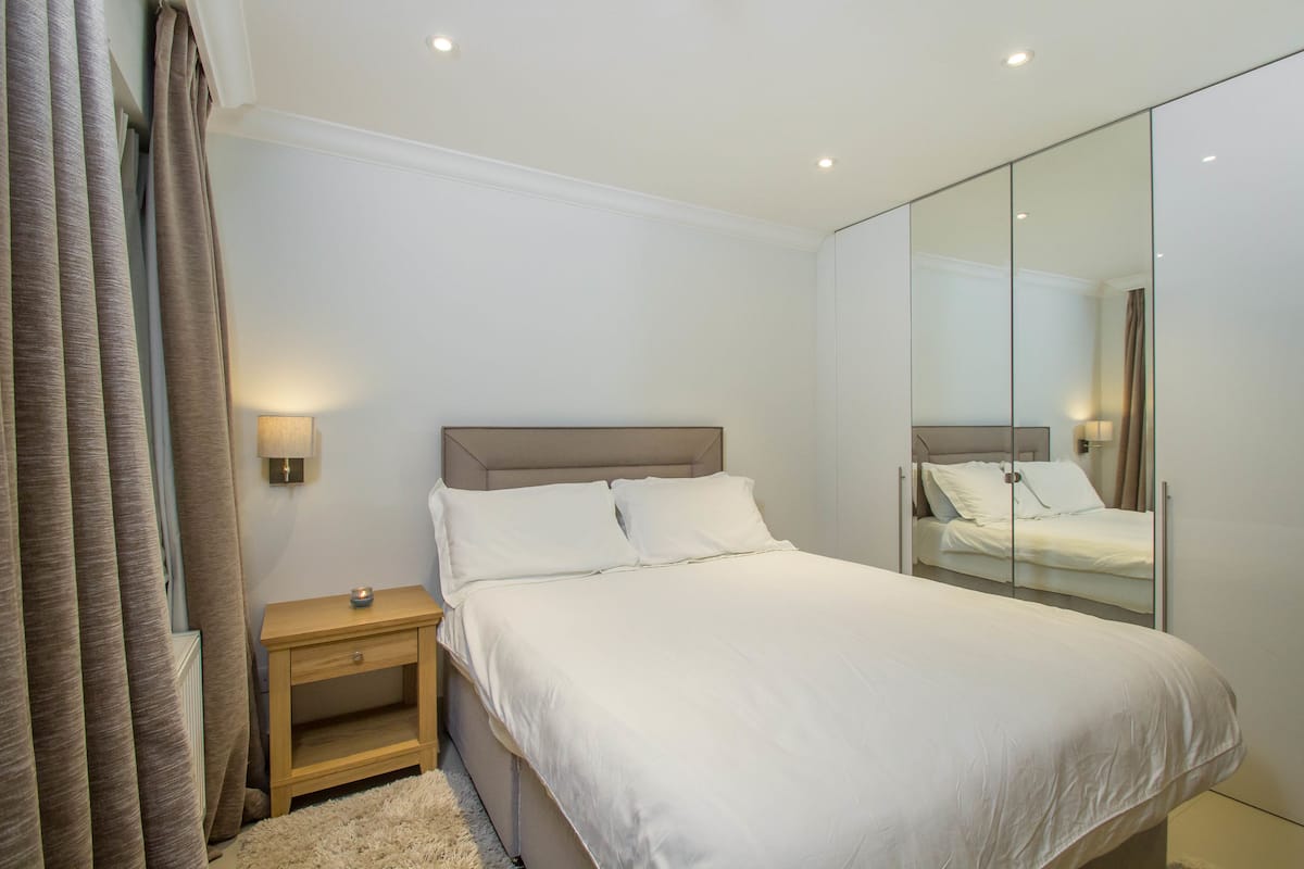 A bedroom with a bed, nightstand, and mirror.