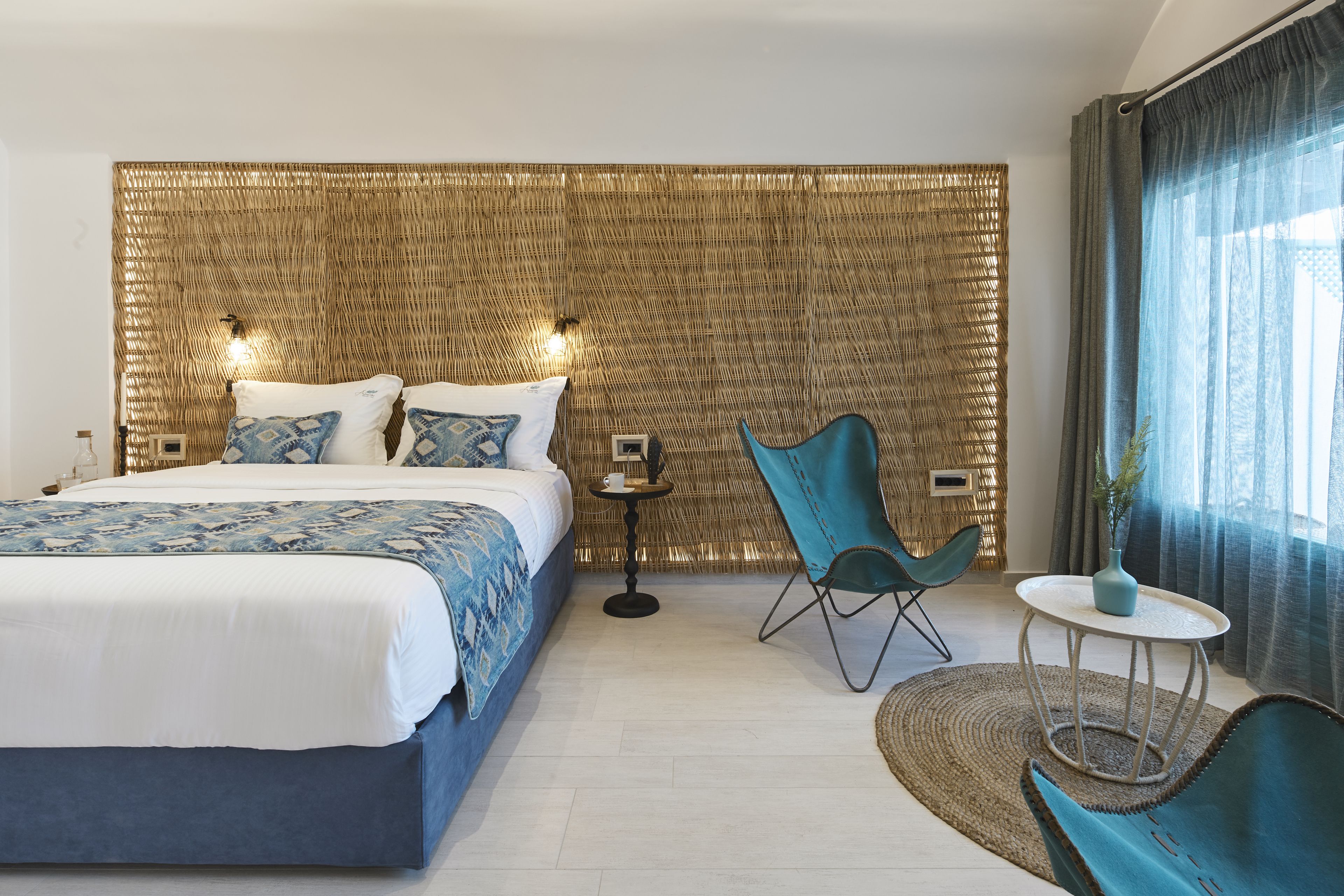 A modern bedroom with a large bed, a small round table, two chairs, and a decorative wall panel.