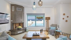 Una sala de estar moderna con chimenea, un ventanal con vistas al mar, una mesa de comedor y un rincón de estar acogedor.