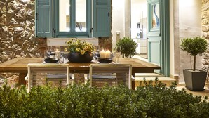 Una mesa de comedor decorada con velas, flores y copas, con paredes de piedra y contraventanas de madera al fondo.