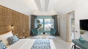 Una habitación de hotel moderna con una cama grande, dos sillas junto a una ventana, una mesita y un televisor en la pared.