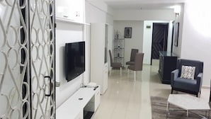 A modern living room with a flat-screen TV, a white entertainment unit, two armchairs, and a coffee table. - Résidence Villa Blanche (Abidjan)
