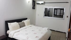 A bedroom with a bed, a nightstand, an air conditioning unit, a window, and a wall-mounted light fixture. - Résidence Villa Blanche (Abidjan)
