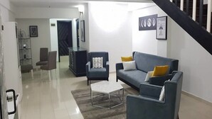 A modern living room with a sofa, armchairs, and a coffee table. A staircase is visible in the background. - Résidence Villa Blanche (Abidjan)