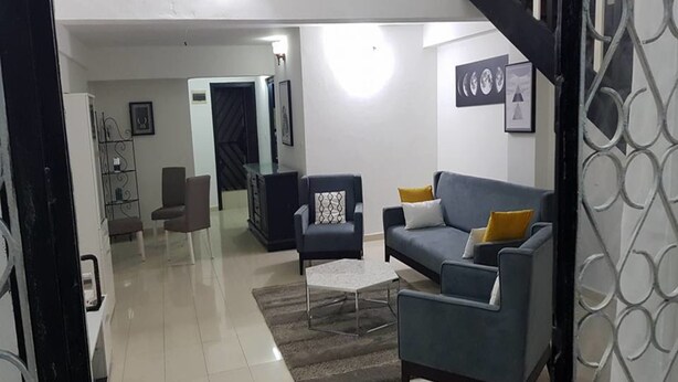 A modern living room with a blue sofa, a coffee table, and a patterned rug. There is a staircase with a black railing leading to another level. - Résidence Villa Blanche (Abidjan)
