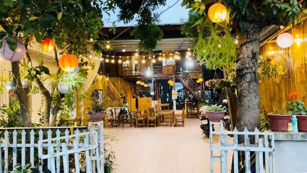 An outdoor seating area with tables and chairs, surrounded by potted plants and string lights.