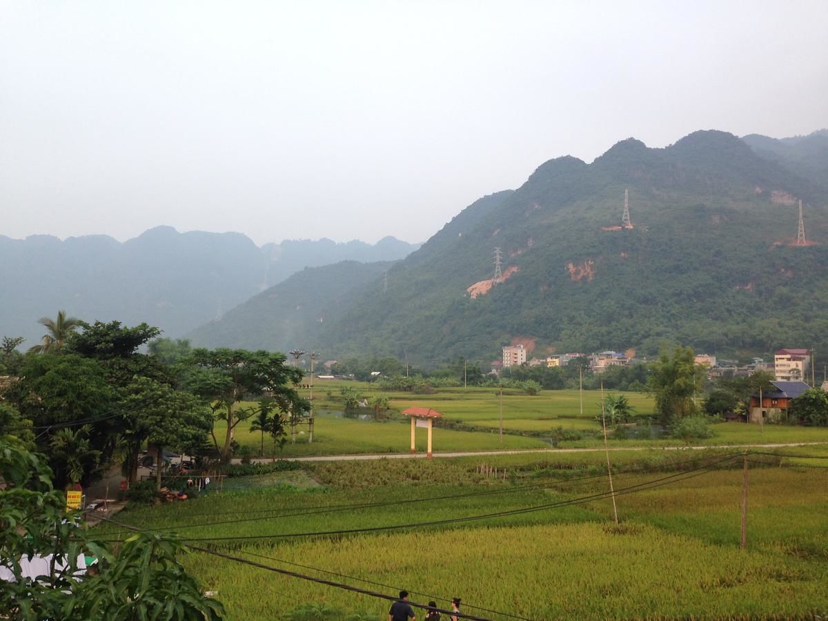 A rural landscape with green fields, a small structure, and distant mountains.