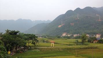 A rural landscape with green fields, a small structure, and distant mountains.