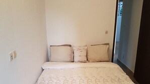 A small, single-bed room with a white bedspread and matching pillows. - Résidence Marié Majeur (Abidjan)