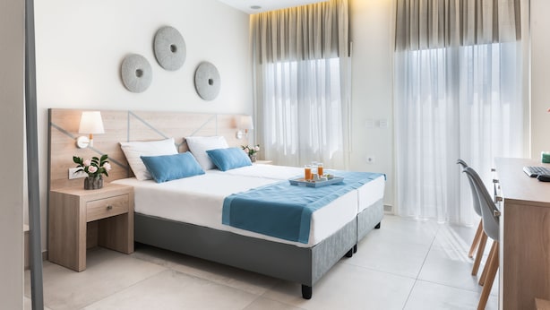 A modern bedroom with a bed, bedside tables, a desk, and curtains. - Santorini Main Square (Santorini)
