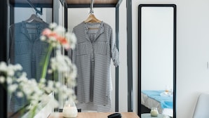 A modern hotel room with a wooden desk, a black keyboard, a teal vase, and a hanging garment rack with striped clothing. - Santorini Main Square (Santorini)
