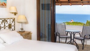 A bedroom with a bed, bedside lamps, a nightstand, and a view of the sea through a glass door. - Leandros Hotel (Aristotelis)